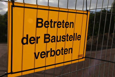 Close-up of yellow warning sign on metal gate