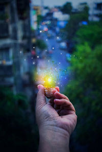 Digital composite image of hand holding illuminated light bulb