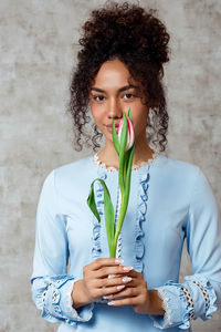 Portrait of beautiful woman holding tulip while standing against wall