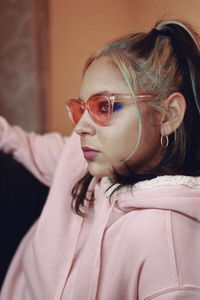 Young woman wearing sunglasses looking away while sitting against wall at home