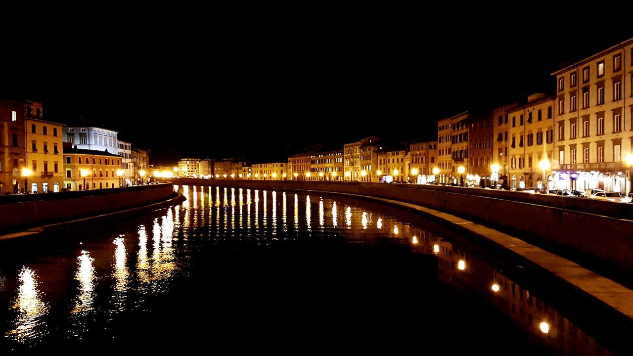 ILLUMINATED CITY BY RIVER AGAINST SKY AT NIGHT