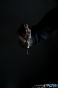 Cropped hand of man holding honey dripper against black background
