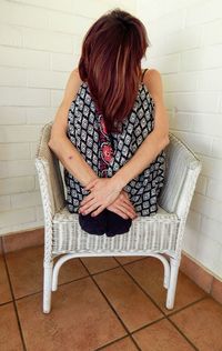 Full length of woman sitting on chair against wall