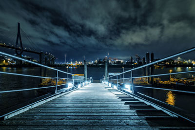 Illuminated bridge over river against cloudy sky at night