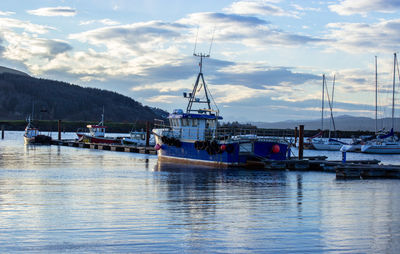 Boats moored in river against cloudy sky at dusk