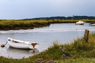 Boats in river amidst field against sky