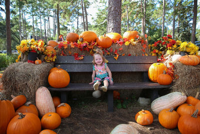 Girl sitting on bench amidst pumpkins at park during autumn