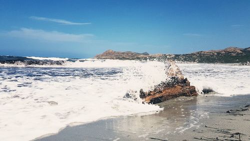 Scenic view of sea waves splashing on shore against sky