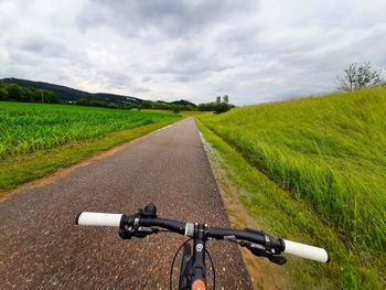 Bicycle on road amidst field against sky