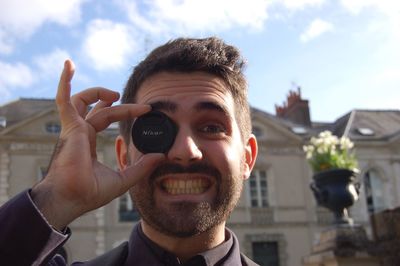 Portrait of man covering eye with lid in city against sky