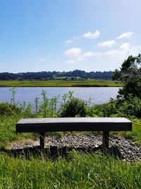 Park bench by lake against sky