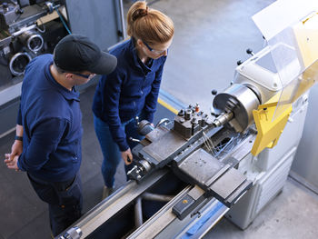Instructor explaining trainee over lathe machine in industry
