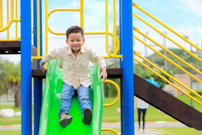 Portrait of cute boy sliding on slide in park