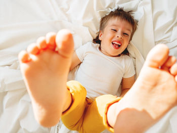 Little boy is lying upside down on bed laughing happily. playful child shows his feet in the air.