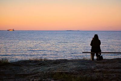 Rear view of woman sitting on bench at beach during sunset