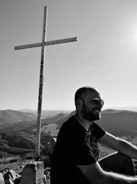 Smiling man by cross looking away against mountain and sky