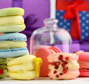 Baked macarons with different flavors and rosebuds on a white background, behind gift boxes, clos