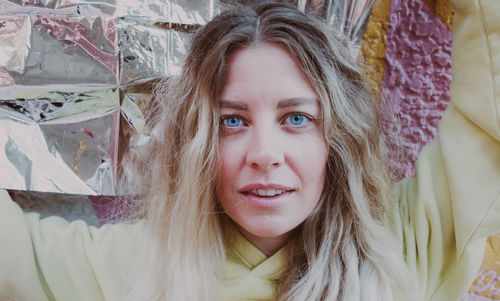 Woman with blonde hair, blue eyes wearing yellow shirt, reflective foil surface, looking into camera