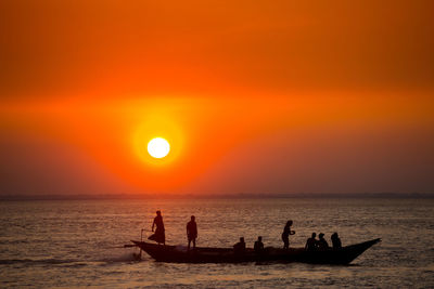 Silhouette people in sea against sky during sunset