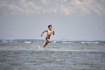 Full length of shirtless boy at beach against sky