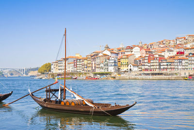 Sailboat on sea by buildings against clear sky