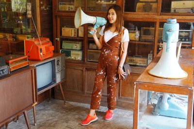 Young woman holding megaphone while standing in antique store