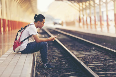 Side view of teenage boy using phone while sitting at railroad station platform