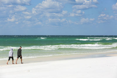 Rear view of men walking on beach against sky