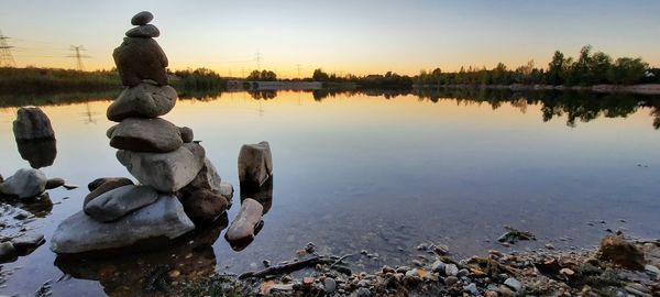 Stack of rocks by lake against sky during sunset