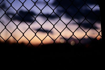 Close-up of chainlink fence against sky during sunset