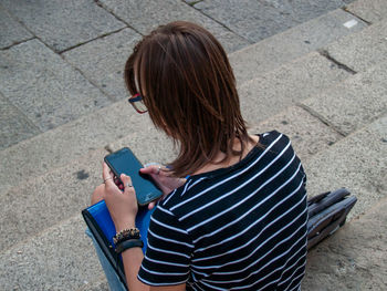 Rear view of teenage girl using mobile phone while sitting on steps