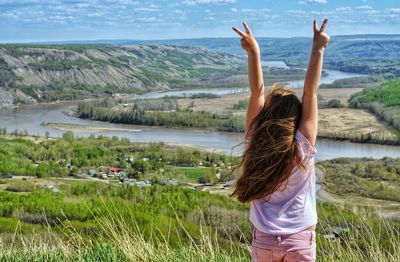 Rear view of woman with hands raised gesturing peace sign against landscape