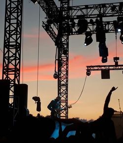 Silhouette people at amusement park against sky during sunset