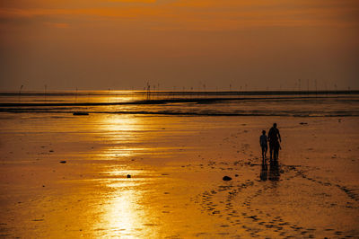 Silhouette people walking on beach against sky during sunset