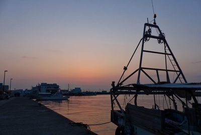 Silhouette cranes at harbor against clear sky at sunset