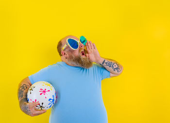Man wearing sunglasses standing against yellow wall