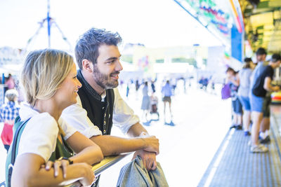 Smiling man and woman looking away while leaning on railing at event