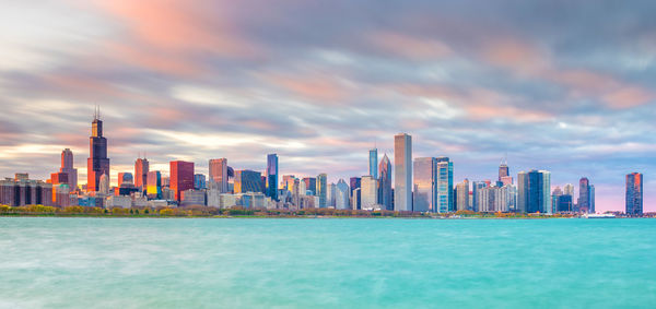 Sea and buildings in city against cloudy sky