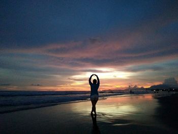 Silhouette woman standing at beach against sky during sunset