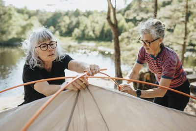 Two senior women setting up tent at campsite at lakeshore