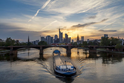 Bridge over river by buildings against sky during sunset