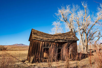Abandoned house on field against clear blue sky