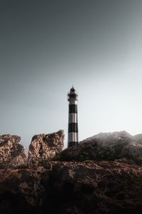 Lighthouse on rock by building against clear sky