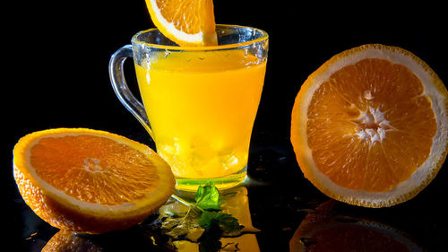 Glass with orange juice, orange halves and mint on a black background, copy space, levitation