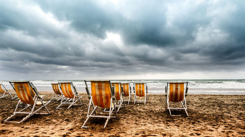 Deck chairs at beach against cloudy sky