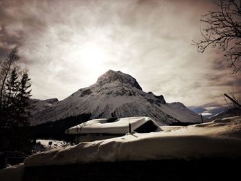 Snow covered house by mountain against sky