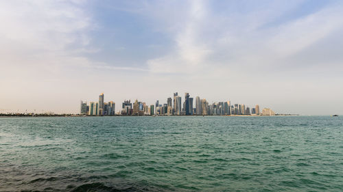 Sea by buildings in city against sky