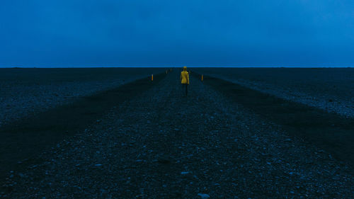 Hiker in bright yellow coat walked down the volcanic black sand path