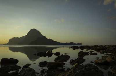 Rocks by sea against sky during sunset