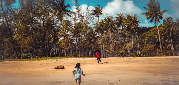 Rear view of people walking on sand against trees at beach